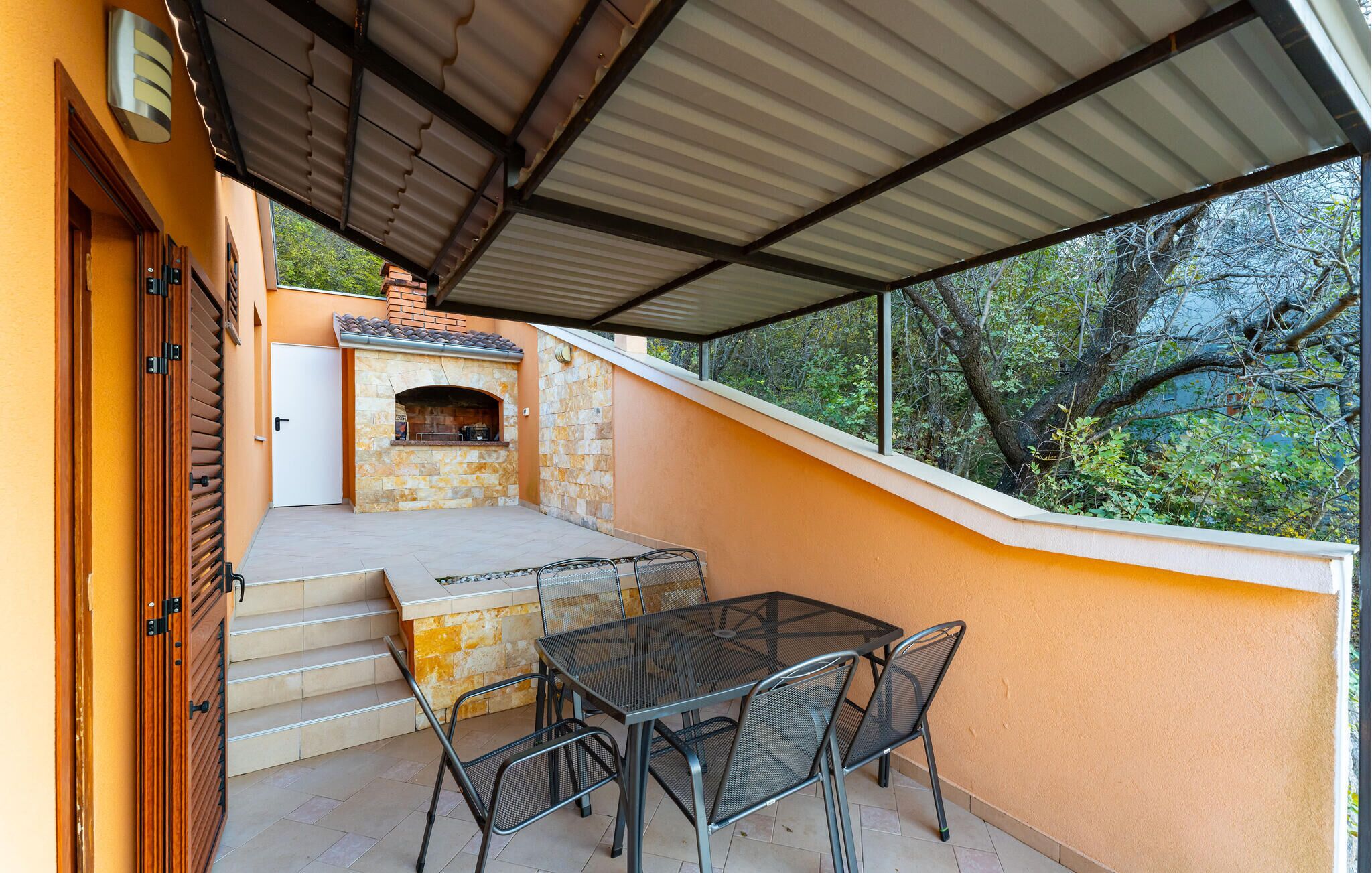 An outdoor patio with a stone fireplace, a table and chairs, and a covered area with a metal roof.