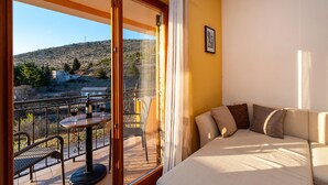 Una stanza con balcone, un divano, un tavolo con bicchieri da vino e una bottiglia, e vista su un paesaggio collinare.