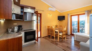 Una cucina compatta con elettrodomestici moderni, una zona pranzo con sedie in legno, una TV a schermo piatto e un balcone con vista.