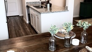 A modern kitchen with a central island, a chandelier, and a dining area with a wooden table and woven placemats.