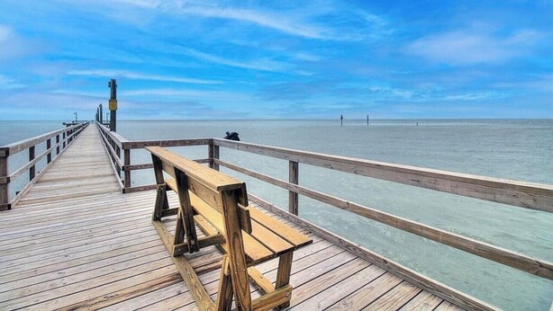 A wooden pier extending into calm waters with a bench and a person standing at the end.