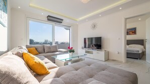Una sala de estar moderna con sofá, una mesita de centro de vidrio, televisor y cama.