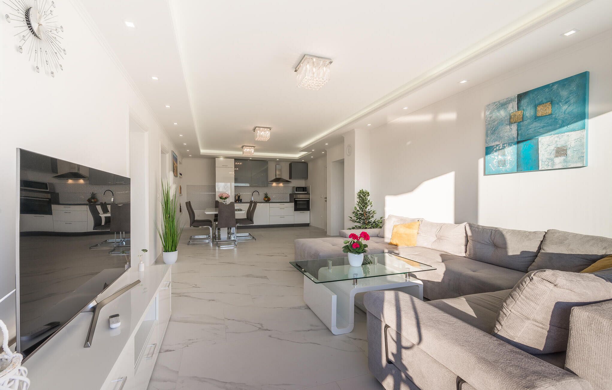Un salon moderne avec une table basse en verre, un canapé gris et un coin repas comprenant une table et des chaises blanches.