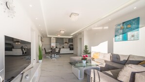 Una sala de estar moderna con una mesa de centro de vidrio, un sofá gris y un comedor con una mesa y sillas blancas.