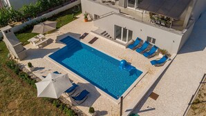 Una piscina con sillas de descanso y sombrillas, rodeada por un patio de piedra y un edificio con ventanas amplias.