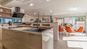 A modern kitchen with a central island, built-in appliances, and a dining area with orange chairs.