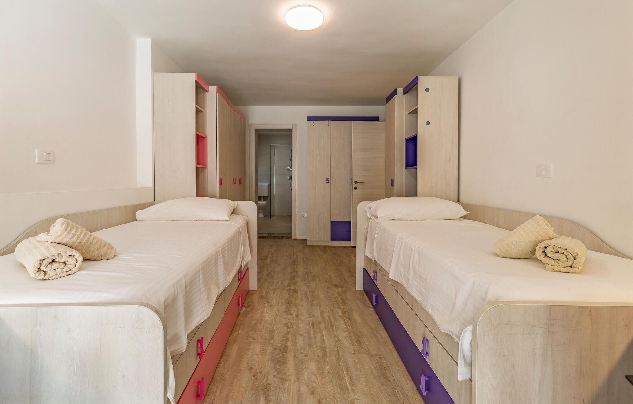 A hotel room with two beds, a wardrobe, and a bathroom visible through an open door.