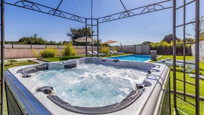 A hot tub with a view of a backyard pool and a clear blue sky.