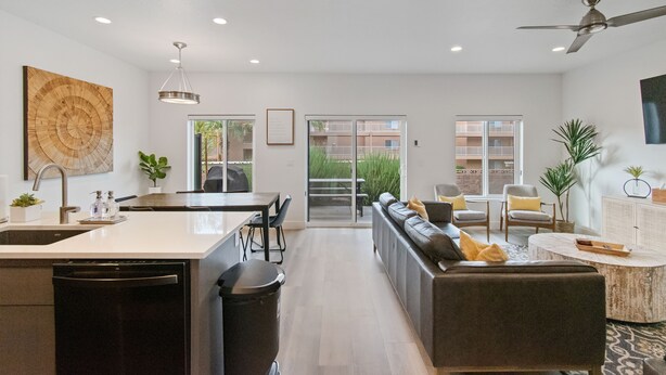 A modern kitchen with a central island, a dining area with a table and chairs, a living room with a sofa and chairs, and a large window with a view of the outside. - Luxury 5-Bed, 5-Bath Townhome - 3 King Suites + Bunks - Heated Pool & Hot Tub (St. George)