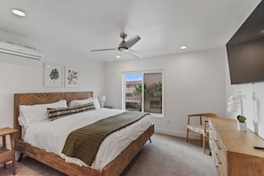 Quarto com cama, escrivaninha, cadeira, ventilador de teto e janela com vista para edifícios.