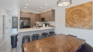 A modern kitchen with wooden cabinets, a stainless steel refrigerator, and a large wooden dining table with bar stools. - Luxury 5-Bed, 5-Bath Townhome - 3 King Suites + Bunks - Heated Pool & Hot Tub (St. George)