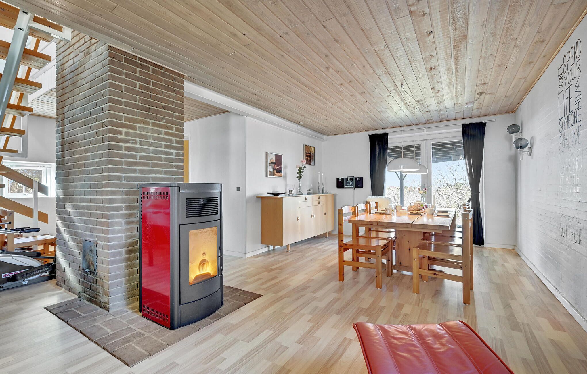 Une cuisine moderne avec un poêle à bois, un coin repas avec une table et des chaises en bois, et un escalier avec une rampe en bois.