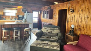 L’intérieur d’un chalet rustique comprend un coin repas en bois, des tabourets de bar, un canapé et un fauteuil rouge.
