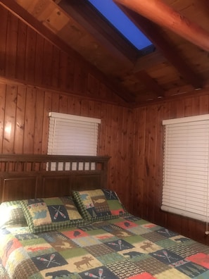 Een slaapkamer in een houten blokhut met een schuine plafond, dakraam en een bed met een kleurrijke quilt.