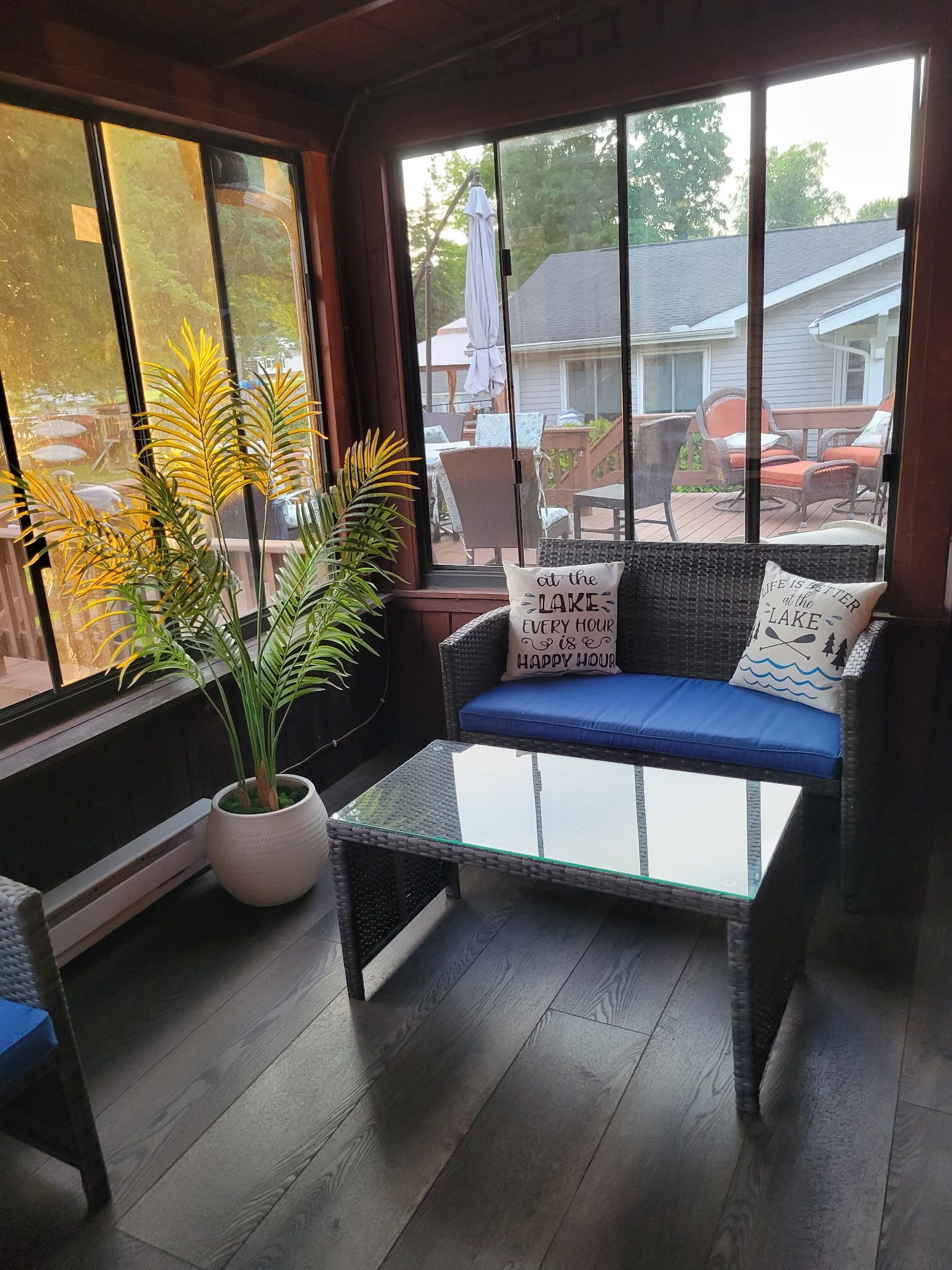 A sunroom with a glass table, wicker sofa, and potted plants.