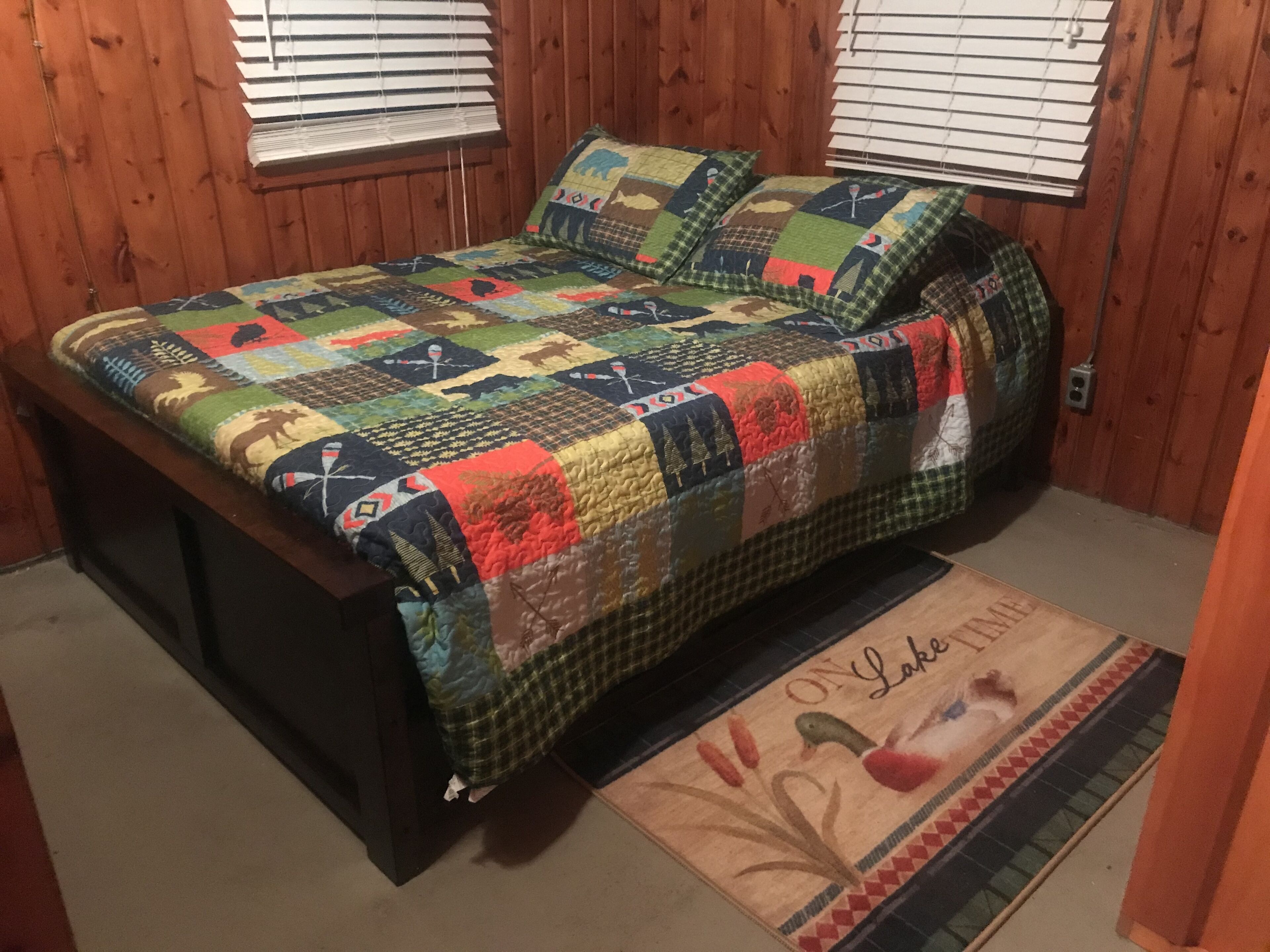 A bedroom with a wooden bed, a colorful quilt, and a rug with a duck design.