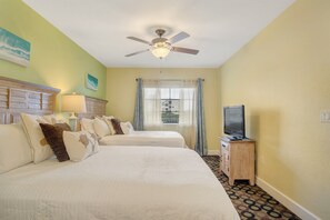 A hotel room with two beds, a ceiling fan, a television on a wooden cabinet, and a window with curtains.