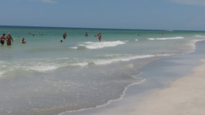 Una playa con gente nadando y caminando por la orilla.