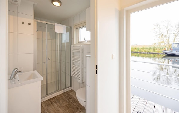 Een moderne badkamer met een douchecabine van glas, een wit wastafelmeubel en uitzicht op een gracht met een boot.