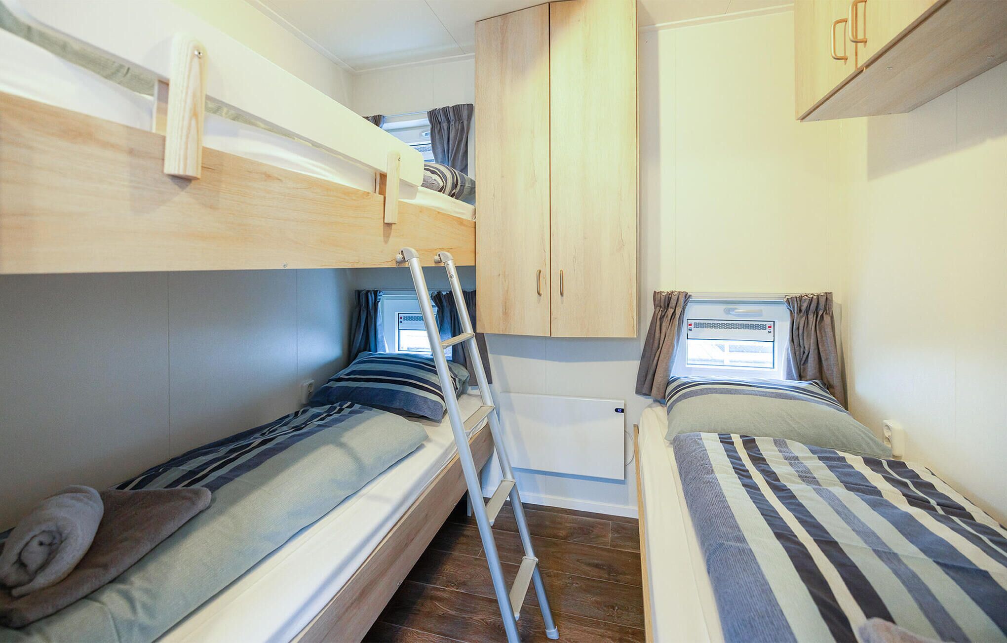 A compact room with bunk beds, a small kitchenette, and a window with curtains.