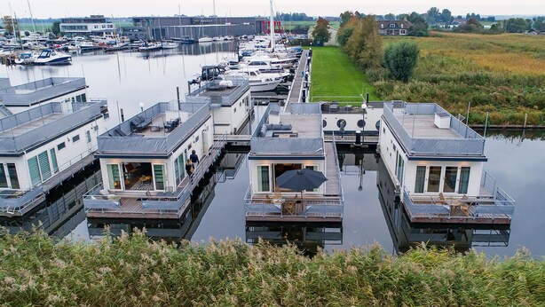 En småbåtshamn med flytande hus, utomhusmöbler och utsikt över vattnet.
