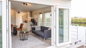 Ett modernt, öppet vardagsrum med en grå soffa, ett litet runt bord och ett köksområde som syns genom en öppen dörr.
