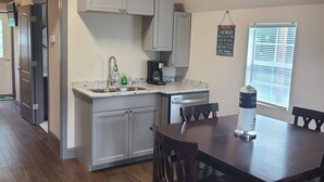 A kitchen with a granite countertop, stainless steel sink, and a coffee maker. There is a dining table with chairs and a window with blinds. - The Corner Shed- Norris Lake or the Mountains (Jacksboro)