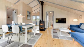 A spacious living area with a high ceiling, a central fireplace, a dining table with chairs, a sofa, and a television mounted on the wall. - Lovely home in Broager with WiFi (Broager)