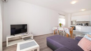 A modern living room with a flat-screen TV, a sofa, a coffee table, and a dining area with a table and chairs. - 2 bedroom awesome apartment in Rovanjska (Rovanjska)