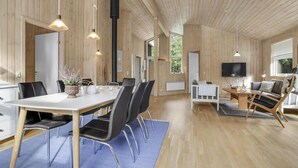 Een ruime kamer met houten inrichting, een zithoek met een witte tafel en zwarte stoelen, een bank en een televisie.