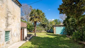 A courtyard with a stone building, a palm tree, and a blue door. - Beautiful home in Nerezine (Nerezine)