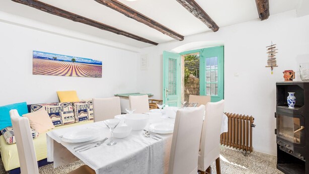 A dining area with a table set for four, a sofa with patterned cushions, a rustic wooden ceiling, and a painting of a field on the wall. - Beautiful home in Nerezine (Nerezine)