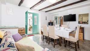 A dining area with a table set for four, a television mounted on the wall, and a door leading to an outdoor area. - Beautiful home in Nerezine (Nerezine)