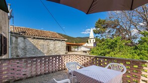 A terrace with a table and chairs, a brick wall, and a view of a church and mountains. - Beautiful home in Nerezine (Nerezine)