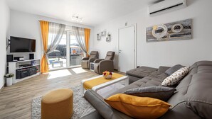 Ein modernes Wohnzimmer mit Sofa, Sesseln, einem Fernseher und einem Essbereich mit Tisch und Stühlen.