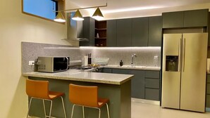 A modern kitchen with a central island, bar stools, a stainless steel refrigerator, and pendant lighting.