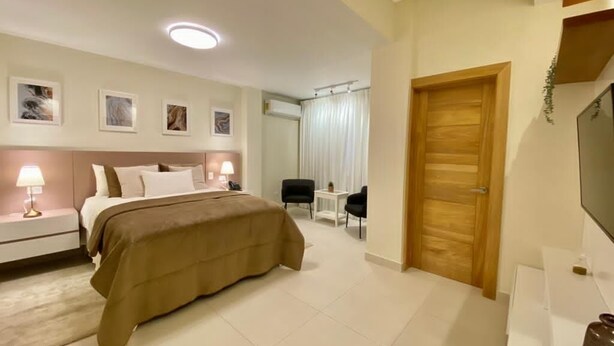 A hotel room with a bed, bedside tables, a desk, a chair, a TV, and a door.