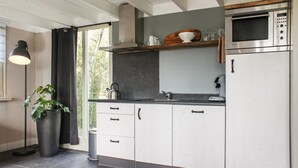 Une cuisine moderne avec des meubles blancs, un four à micro-ondes en acier inoxydable, une bouilloire et une plante en pot.
