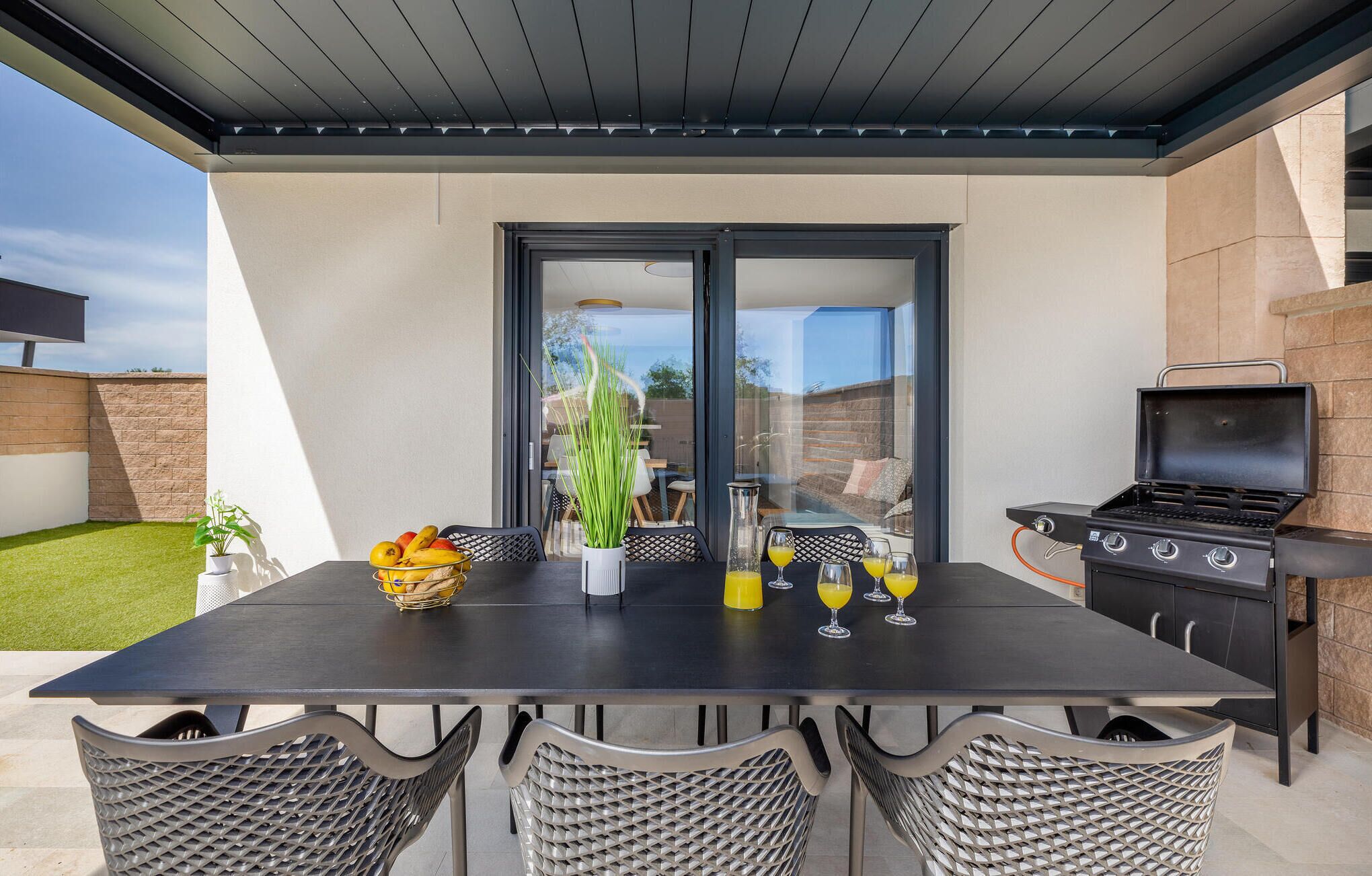 An outdoor patio with a table set for two, a grill, and a view of the backyard.