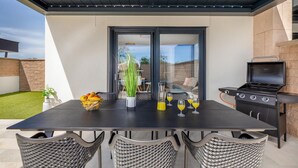 Una veranda esterna con un tavolo apparecchiato per due, un barbecue e vista sul giardino.