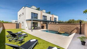 Una moderna casa a due piani con piscina, area salotto esterna e prato curato.
