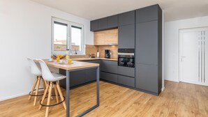 Una cucina moderna con mobili grigi, un piano di lavoro in legno e un piccolo angolo pranzo con due sedie bianche.