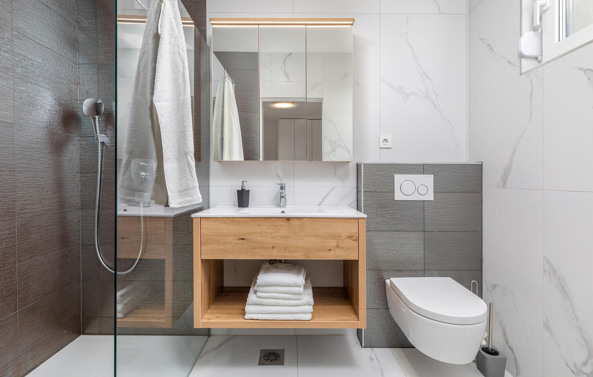 A modern bathroom with a glass shower enclosure, a wooden vanity with a sink, and a toilet.