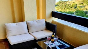 Un balcon agrémenté de meubles en osier, d’une table en verre et d’une bouteille de vin.