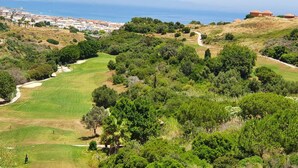 Un parcours de golf offrant une vue sur une ville côtière et des montagnes à l’horizon.