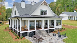 A two-story house with a covered porch, stone patio, and outdoor seating area.