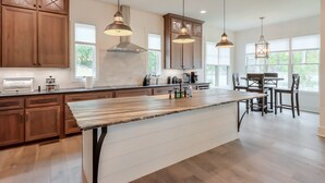 A spacious kitchen with wooden cabinets, a large island, pendant lighting, and a dining area with chairs.