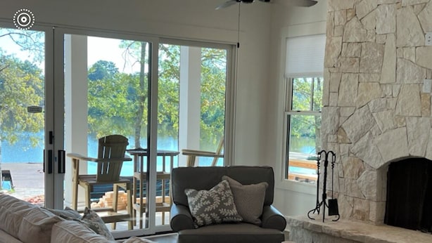 A living room with a stone fireplace, a sofa, and a view of a lake through large sliding glass doors.