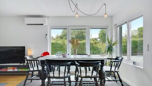 Ein Essbereich mit einem runden Tisch, sechs Stühlen, einem Fernseher und einem großen Fenster mit Blick ins Grüne.