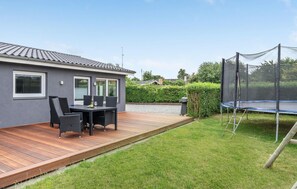 Ein modernes Haus mit einer Holzterrasse, einem Trampolin und einem Patio-Tisch mit Stühlen.